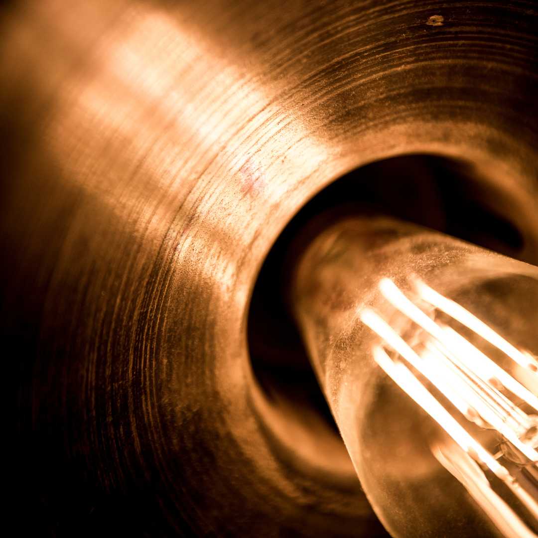 Illuminated filament bulb being reflected in a brass lampshade close up.